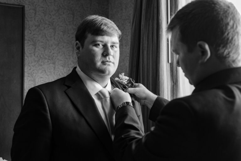 Black and white photo of Dan getting his boutonniere pinned on before his Heritage Hills Golf Resort wedding in York, PA